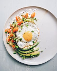 an egg is on top of some veggies on a white plate with sprouts