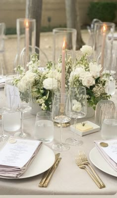 the table is set with white flowers, candles and place settings for an elegant dinner