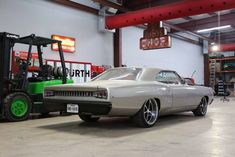 an old car is parked next to a forklift in a garage with other cars