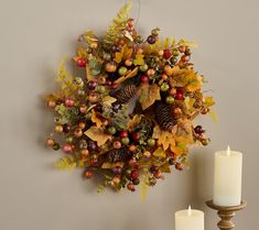 a wreath is hung on the wall next to two candle holders with autumn leaves, berries and acorns