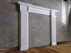 a white fireplace mantel on top of a hard wood floor next to a gray wall