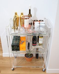 a clear bar cart filled with bottles and glasses on top of a hard wood floor