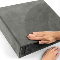 a woman's hand is on the edge of a gray book with engraved lettering