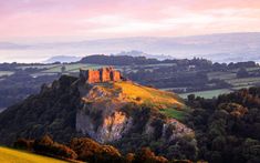 a castle on top of a hill with trees around it and mountains in the background