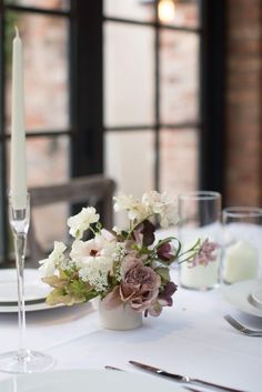 the table is set with white and purple flowers, silverware, candles and napkins