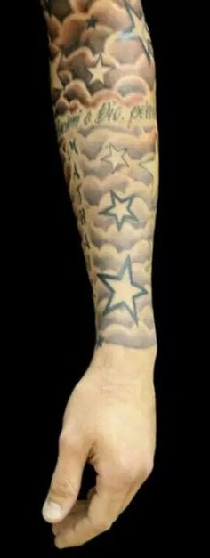 a man's arm with stars and clouds tattooed on the sleeve, in black background