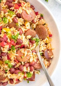 a white bowl filled with rice, sausage and veggies next to a fork