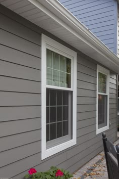 a patio table and chairs in front of a gray house with white trim on the windows