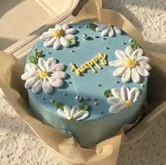 a blue cake decorated with white flowers and the words happy on it is in a box