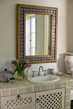 a bathroom sink with a mirror above it and flowers in the vase on the counter