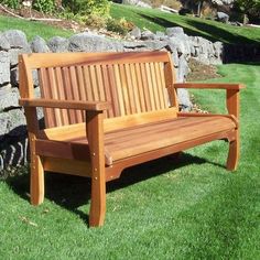 a wooden bench sitting in the grass next to a rock wall and stone wall behind it