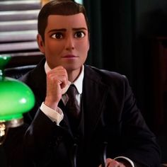 a man in a suit and tie sitting at a desk with a green lamp behind him