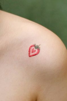 a small strawberry tattoo on the back of a woman's left shoulder and chest