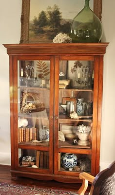 an antique china cabinet with glass doors and shelves filled with vases, books, and other decorative items