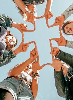 a group of people standing in a circle holding their hands together and making a heart shape