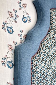 the back end of a blue couch next to a white wall with floral designs on it