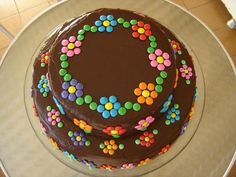 a chocolate cake decorated with colorful candies on a white platter in front of a tiled floor