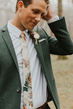 a man in a suit and tie is holding his hand to his ear while wearing a flower boutonniere