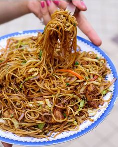 someone is holding a plate of noodles with chopsticks