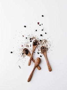 two wooden spoons filled with spices on top of a white table next to black pepper flakes