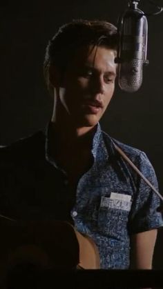 a young man is playing the guitar in front of a microphone while singing into a mic