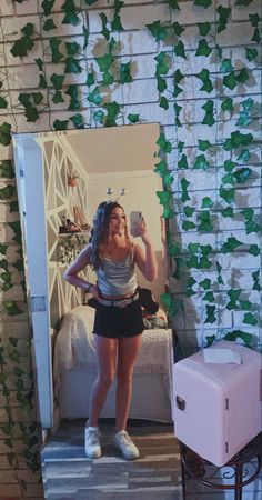 a woman taking a selfie in front of a mirror with ivy growing on it