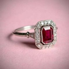 an engagement ring with a large red stone surrounded by small white diamonds on a pink background