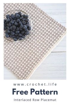 a bowl of blueberries sitting on top of a table next to a knitted placemat