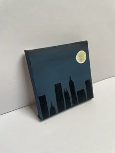 a painting of a city at night with the moon in the sky and buildings painted on it