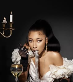 a woman wearing black gloves and holding a wine glass in front of her face while sitting at a table