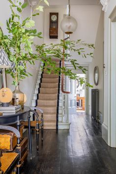 a house with stairs and plants in the entryway, next to a table that has two chairs on it