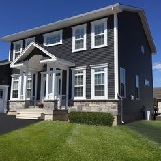 a large gray house with white trim on the front and side windows, grass in front