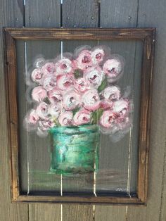 a painting of pink flowers in a green vase on a wooden frame hanging on a fence