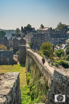 two people walking on a bridge over a small river in the middle of an old town