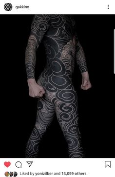 a man with tattoos on his body is standing in the dark, wearing black and white patterned tights