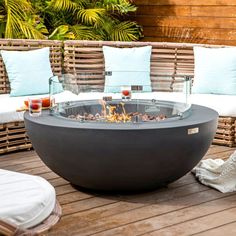 a fire pit sitting on top of a wooden deck next to lounge chairs and pillows