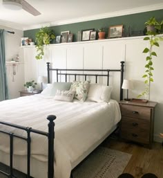 a bed with white sheets and pillows in a bedroom next to a window filled with potted plants