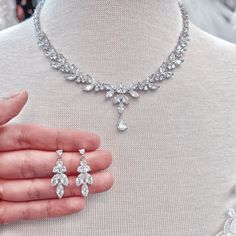 a woman's hand is holding two diamond necklaces and earring on display