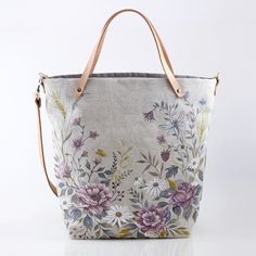 a handbag with flowers painted on the front and side, sitting on a white surface