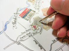 a person holding a pen and drawing on a piece of paper with the city map in the background