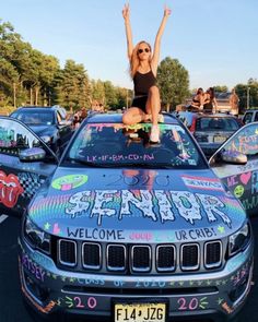 a woman sitting on the hood of a car with her arms up in the air