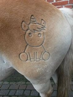 a brown and white horse with a drawing on it's back side standing next to a brick wall