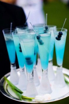 several glasses filled with blue liquid on top of a silver platter and garnished with celery