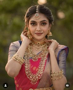 a woman in a red and gold sari with jewelry on her neck, posing for the camera