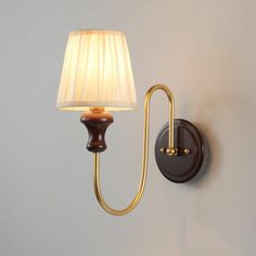 a wall light with a white lamp shade on it's side and a gold arm