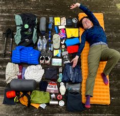 a woman laying on top of an inflatable mattress surrounded by camping gear and items