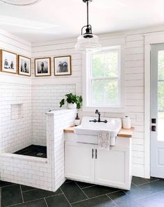 a white bathroom with black tile flooring and pictures on the wall above the sink