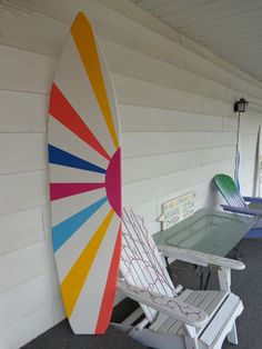 a colorful surfboard sitting on top of a white wall next to a table and chairs