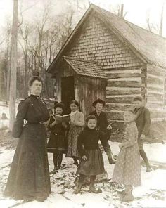 an old black and white photo of people standing in front of a log cabin with snow on the ground