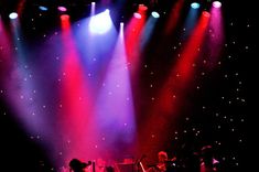 the band is performing on stage with their instruments in front of bright colored spotlights